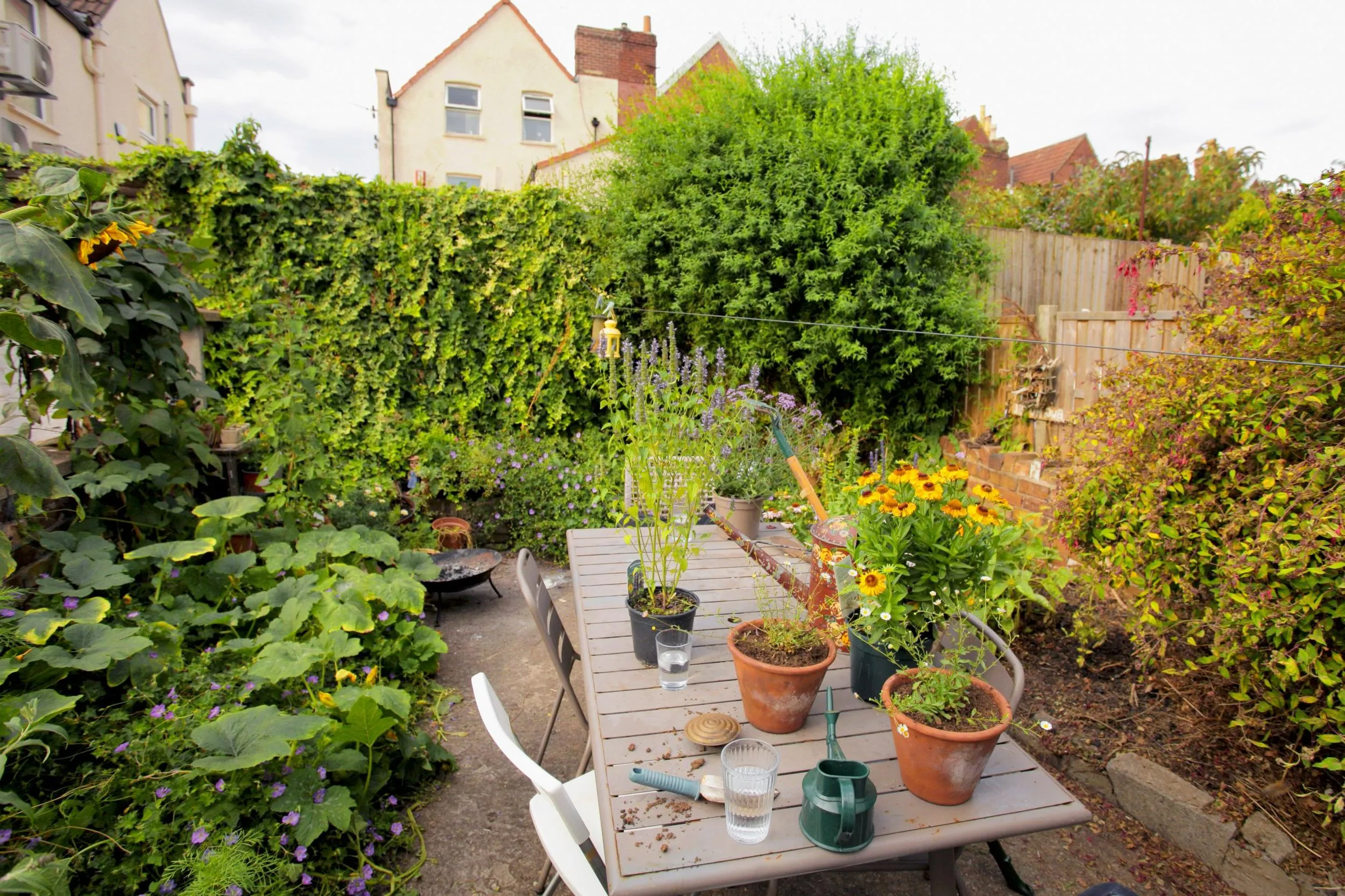 A small but busy garden, with flowerbeds spilling out onto the patio where a table and chairs are set out.